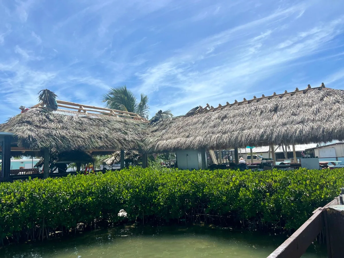 Palm-thatched tiki structures beside waterfront greenery