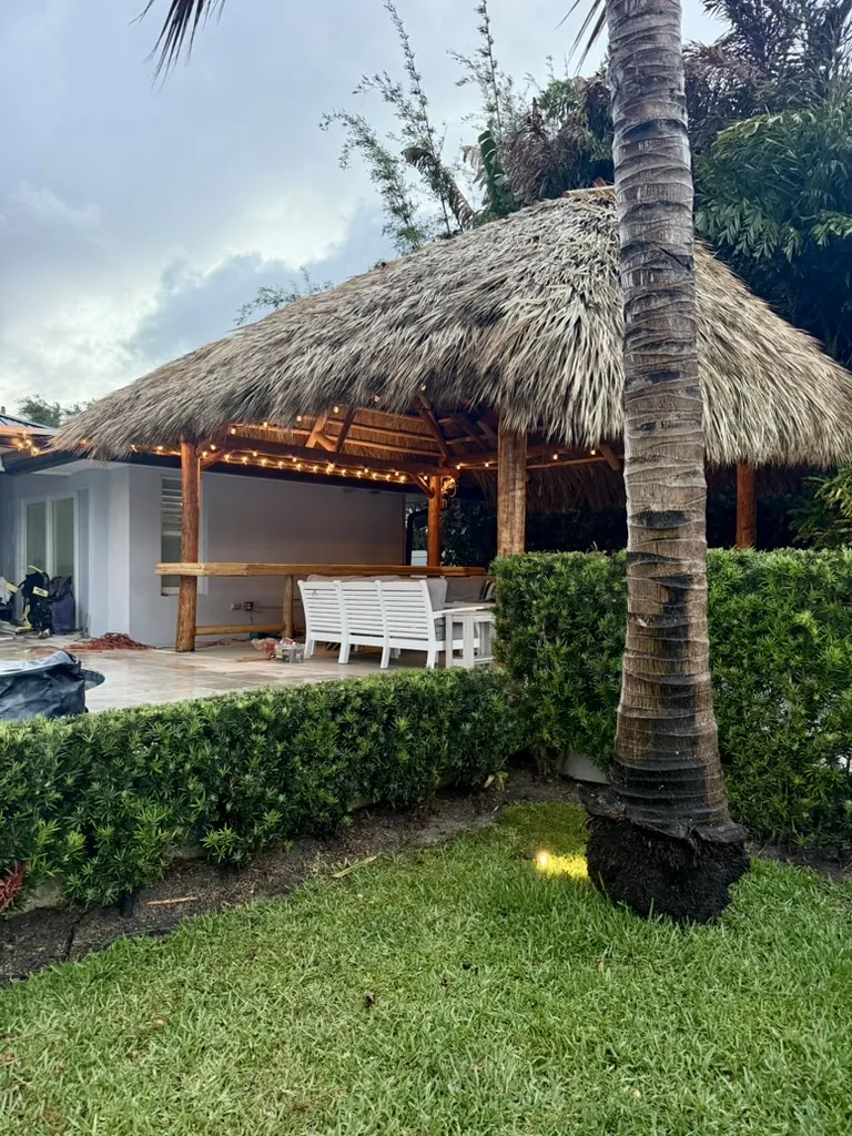 Natural palm tiki hut with warm string lights beside a backyard patio