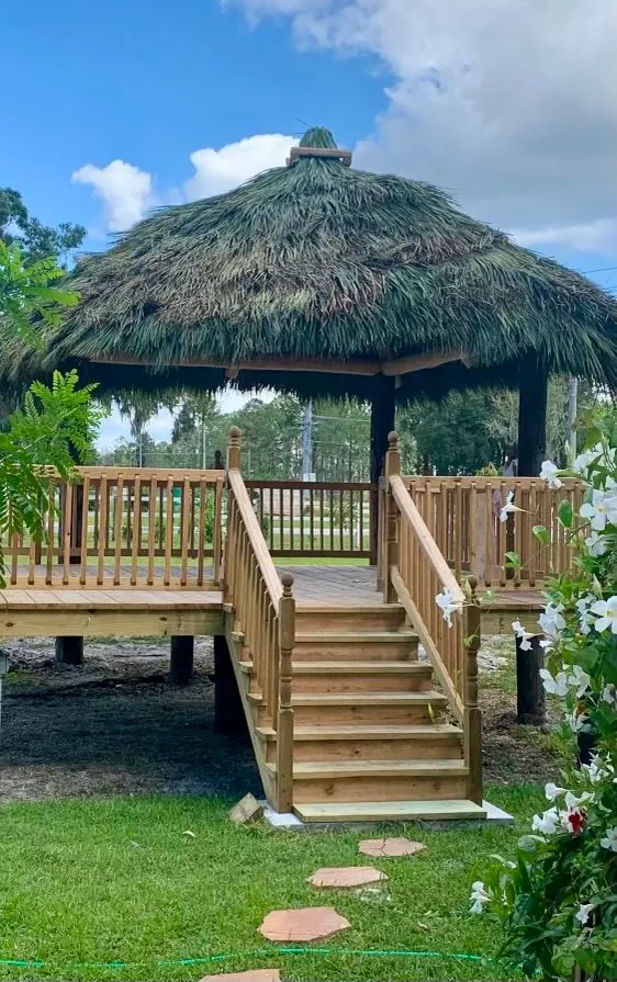 Raised tiki hut with a wooden deck, railings and stairs