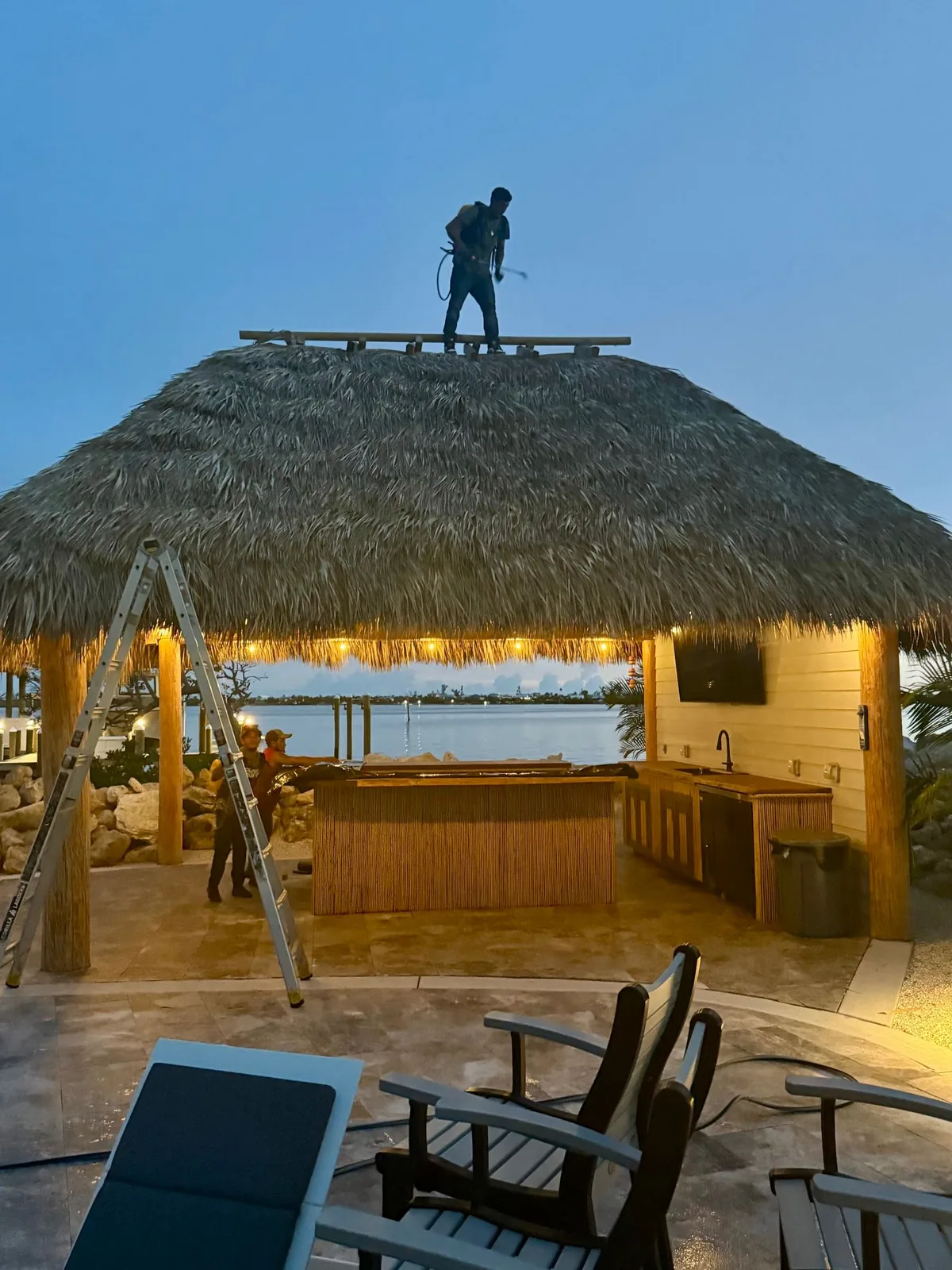 Worker on the roof of a palm-thatched tiki hut at dusk