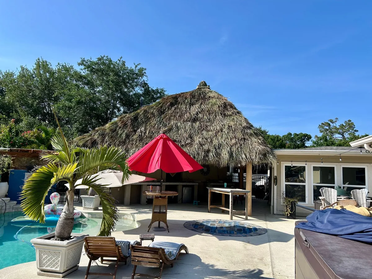 Large palm-thatched tiki hut beside a paved poolside patio