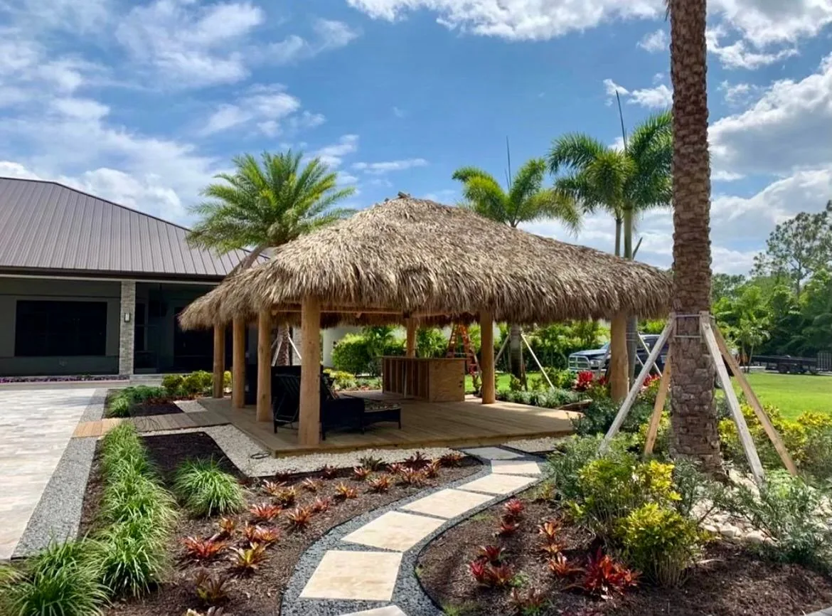 Natural palm tiki hut beside a landscaped backyard patio