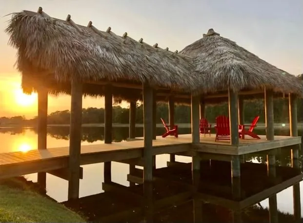 Wooden picnic tables beneath a palm-thatched roof at sunset